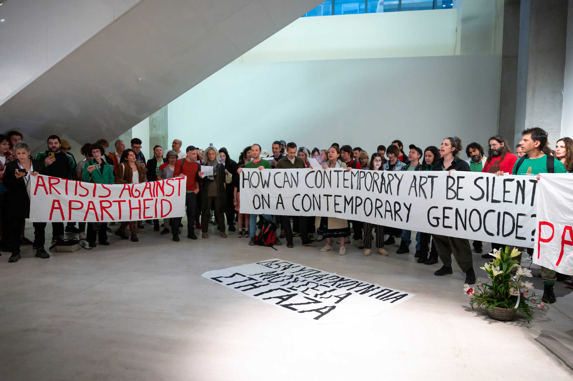 On Friday May 17, 2024 dozens of artists and cultural workers in Athens, Greece, organized a protest at EMST, the museum of contemporary art. The protestors called for EMST to publicly denounce the genocide and culturalcide perpertrated by Israel on the Gazan enclave. The action included the collective reading of the names of  museums, heritage and cultural sites destroyed in Gaza, as well as an extensive list of artists, writers and cultural workers murdered so far. Banners were displayed calling out the art world's silence, and included signs stating "Artists Against Apartheid" and "There are no museums left in Gaza." The protest also called on EMST's current programming on women to acknowledge the 10,300 women killed in Gaza over the past 7 months. Demands included calls for cultural boycott and divestment.